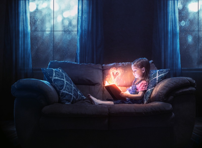 A little girl reading alone with a color heart glowing out of the pages